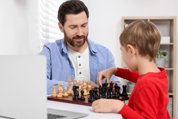 Father and son playing chess following online lesson in room