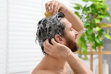 Man washing his hair with solid shampoo bar in bathroom, closeup
