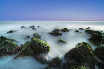 Fototapeta na wymiar Stones and water at twilight allong the sea coast