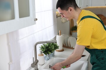 Young plumber wearing uniform repairing sink in kitchen