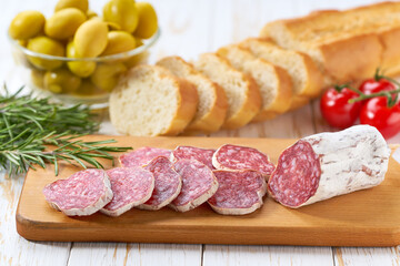 Slices of pork dry cured salami sausage and slices baguette on a wooden table.