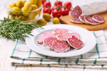 traditional Spanish salami fuet sausage or dry sausage cut in slices on a white ceramic plate, isolated on a kitchen table.