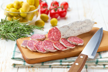 Traditional Spanish fuet spicy pork dry cured salami sausage with rosemary and baguet on a wooden...