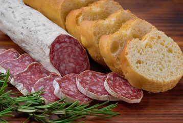 Spanish Fuet sausage salami with rosemary and french baguette on a cutting board.