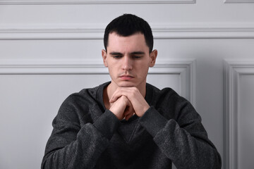 Sad man sitting near white wall indoors