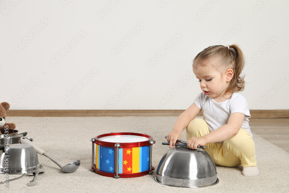 Wall mural Cute little girl with cookware and toy drum at home