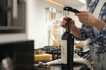 Woman opening wine bottle with corkscrew at black countertop indoors, closeup