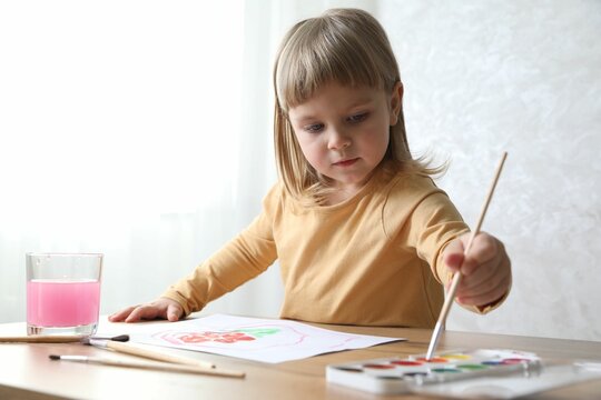 Cute little girl drawing with brush at wooden table indoors. Child`s art