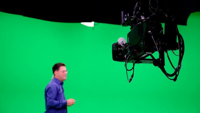 A professional green studio presenter makes an announcement in front of a jimmy jib camera and exits the frame. Chroma Key.