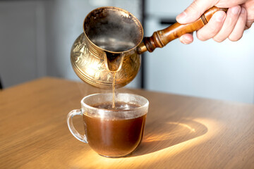 A woman pouring coffee into a cup from a copper Turkish coffee pot