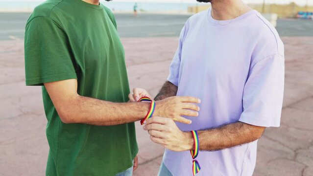 Gay man putting a rainbow bracelet on his male boyfriend to celebrate LGBT pride day parade. Lesbian, gay, bisexual, transgender social movements. Concept of happiness freedom love same-sex couple