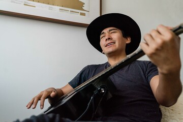 Latin man playing acoustic guitar at home