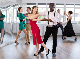 Active young woman training waltz in pair with man in dance-hall during dancing classes