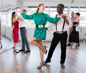 Woman with African man participants of dance workshop perform figure waltz. Students learn to dance...