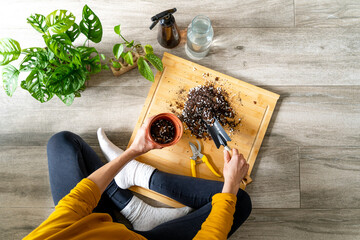 Unrecognizable woman indoors pouring soil into a flower pot.