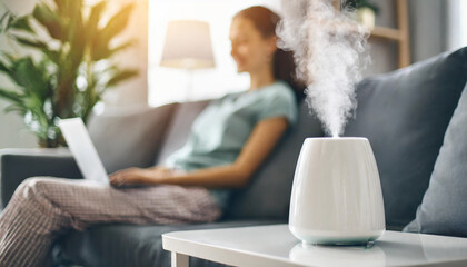 Modern air humidifier on white table with blurred young woman in background, emphasizing indoor comfort and lifestyle - obrazy, fototapety, plakaty
