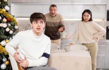 Domestic quarrel during Christmas celebration - father and sister scolding young guy in home kitchen