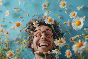 A man with glasses is lying in a field of daisies, he is smiling and has his eyes closed. The background is blue.