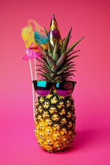 Pineapple wearing sunglasses and party hat on pink background.