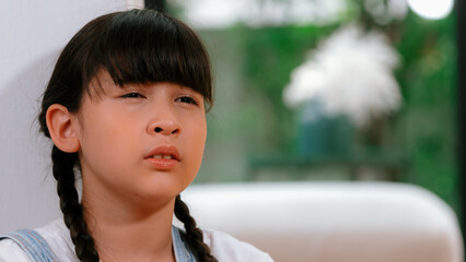 Sad little girl sitting alone in living room crying, feeling lonely. Young girl experiencing social...