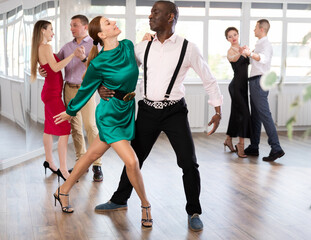 Dynamic middle-aged male and female attendees of dancing courses doing waltz in group