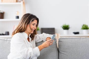 Side view of a mature Woman using mobile sitting on the sofa at home