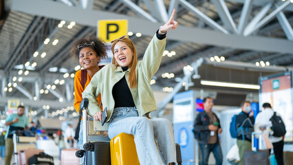 Happy woman friends holding passport and luggage walking together to airline check in counter in...