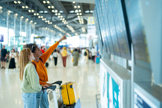 Woman friends looking flight schedule on timetable and go to check-in and boarding gate together in airport terminal. Attractive girl traveler travel by airplane transportation on holiday vacation.