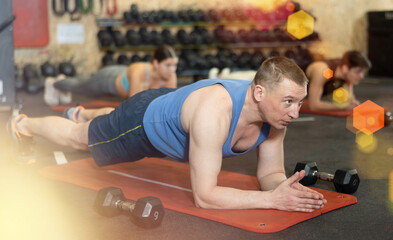 Focused sporty adult man doing bodyweight workout for abdominal and core muscles in gym, holding...