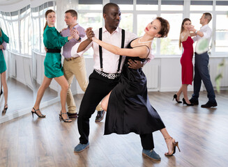 Elegant couple performs an expressive tango in bright, modern dance studio during a group class