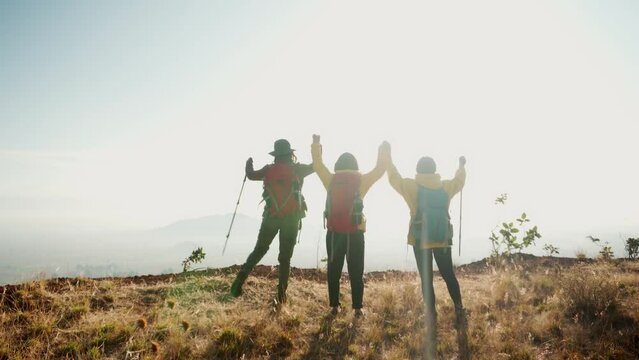 Three friends in yellow jackets and hiking backpacks reach the top of the mountain. Concept of teamwork and self-improvement.