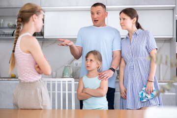 Displeased mother and father reprimanding eldest teenage daughter while standing with her younger...