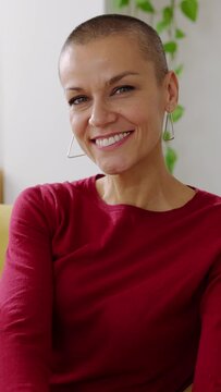 Vertical portrait of mid adult trendy woman looking at camera. Front view portrait of female with shaved head smile relaxing at home. 40s people concept.