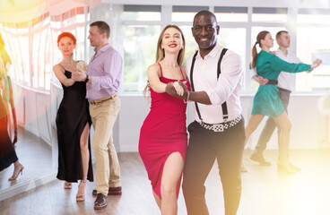 Fototapeta na wymiar With unhurried music, woman with African man in couple spins to rhythm of waltz during lesson for novice students. Classes in mini-groups for those who want to learn dancing