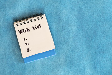 Wish list concept. White note pad isolated on blue background.