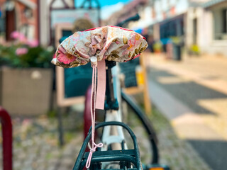 Bicycle parked on a cobblestone city street. The bicycle seat is covered with a beautiful floral-patterned seat cover. Located in Breisach, Germany. - obrazy, fototapety, plakaty