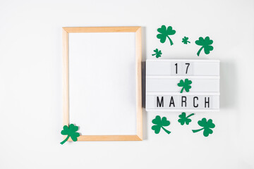 Minimalistic flatlay for St. Patrick's Day. Shamrock and frame on a white background. Happy Irish holiday, symbols of good luck.