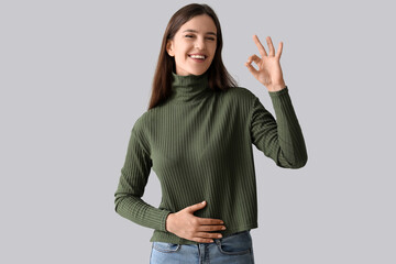 Young woman with healthy stomach showing OK on light background