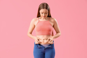 Upset young woman in tight jeans on pink background. Weight gain concept