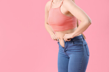 Fototapeta premium Young woman in tight jeans on pink background, closeup. Weight gain concept