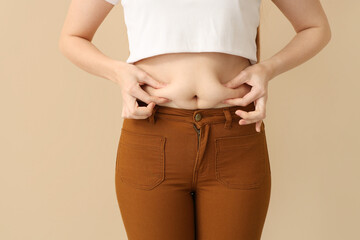 Young woman in tight pants on beige background, closeup. Weight gain concept