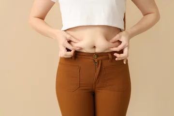 Foto op Plexiglas Young woman in tight pants on beige background, closeup. Weight gain concept © Pixel-Shot