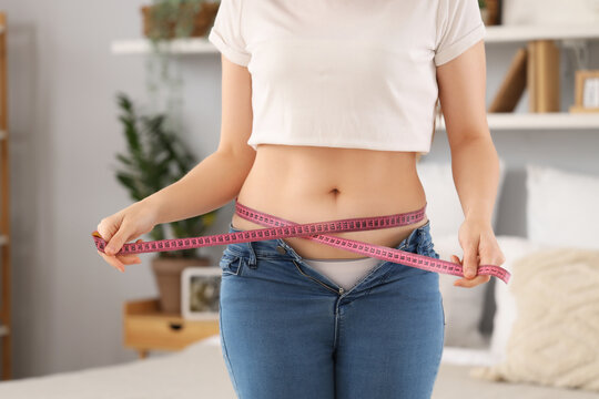 Young woman in tight jeans measuring her belly at home, closeup. Weight gain concept