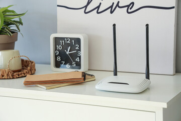 Modern wi-fi router with notebooks and clock on commode in room, closeup
