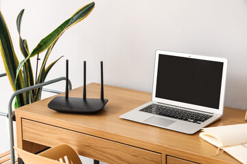 Modern wi-fi router with laptop on table near light wall
