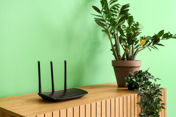 Modern wi-fi router with plants on commode near green wall