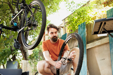 Sporty and dedicated man adjusting bicycle gears with professional equipment in home yard. Active caucasian male repairs and maintains bike components outside using specialized tools.