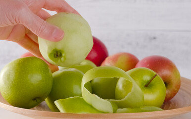 Woman hand holding peeled apple. Apples close-up on a wooden plate