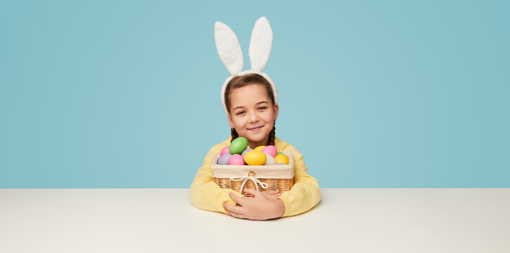 Adorable girl in bunny ears sitting with basket of eggs