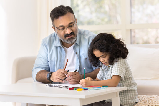 Focused Indian grandfather and cute granddaughter kid drawing creative colorful doodles in paper album together, developing art skills, creativity, hobby, doing school homework